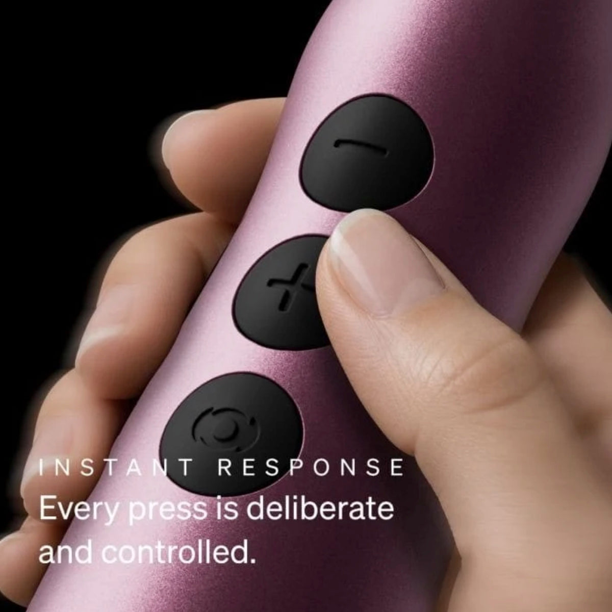 A close-up of a hand holding a metallic pink cylindrical device with three black control buttons, set against a black background with white text reading 'INSTANT RESPONSE Every press is deliberate and controlled.'.